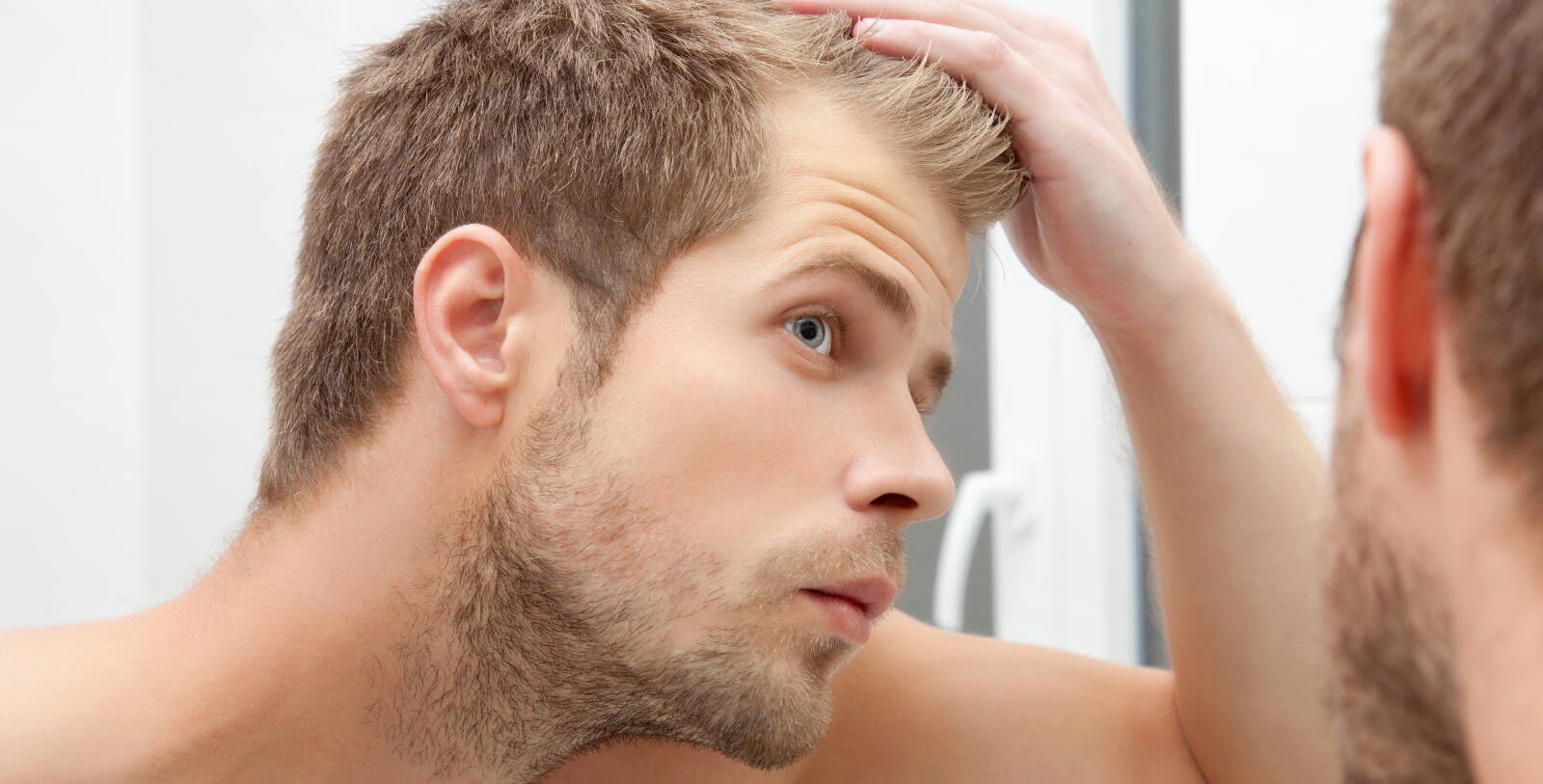 Mann mit vollem Haar, welcher sich im Spiegel anschaut